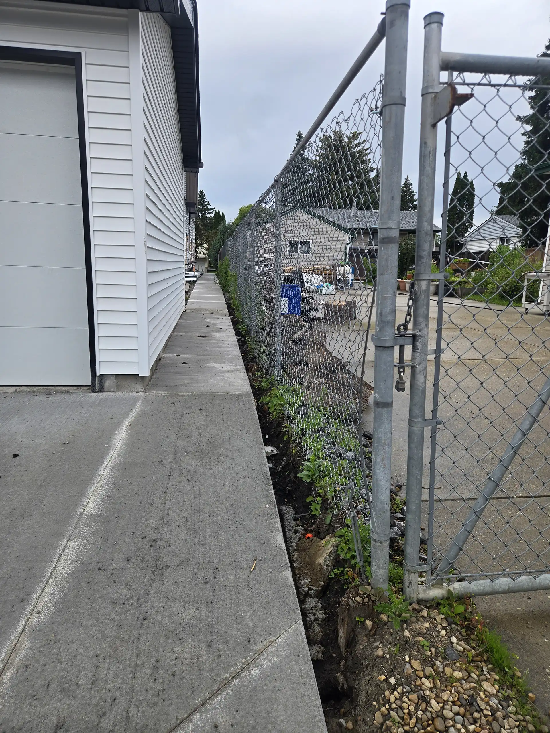 Narrow infill lot side yard with existing chainlink fence limiting space for a retaining wall and drainage swale